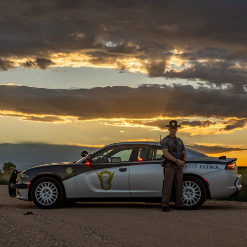 Trooper standing next to patrol car with sunset