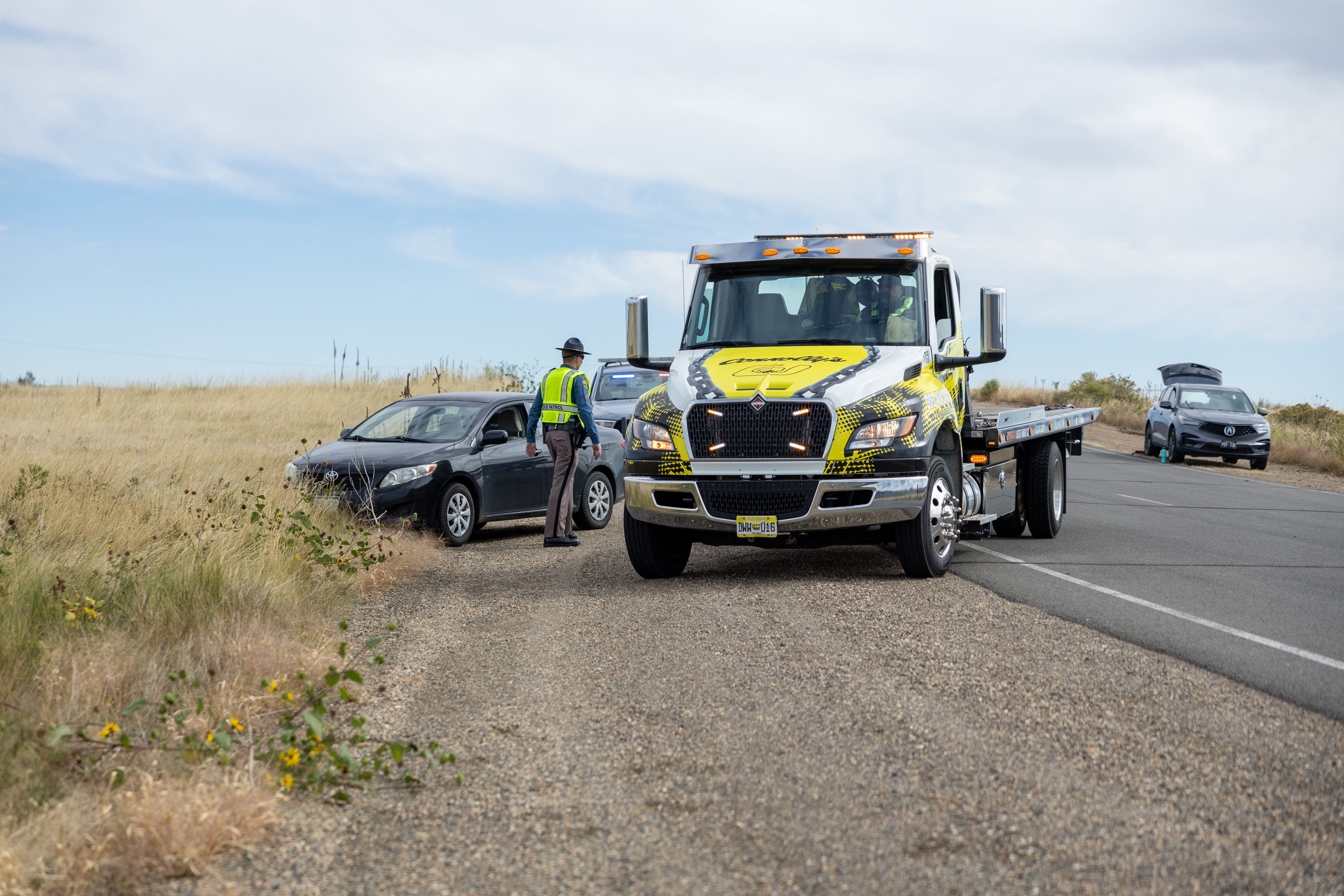 Crashed car with tow truck and trooper working the scene.